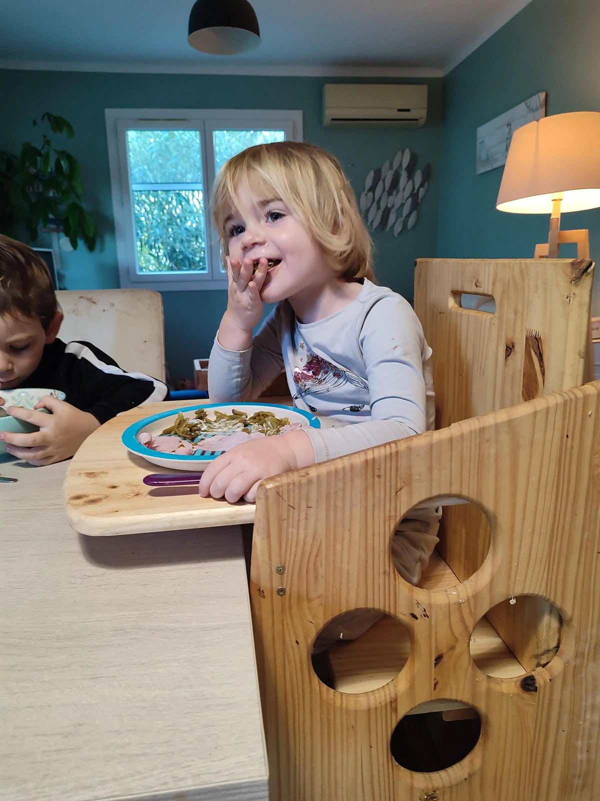 repas pris dans la tour Montessori grâce à son passage en chaise haute avec assise, dossier et plateau repas