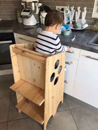 utlisation de la tour MOntessori près du plan de travail de la cuisine avec un dossier à l'arrière pour sécuriser l'enfant