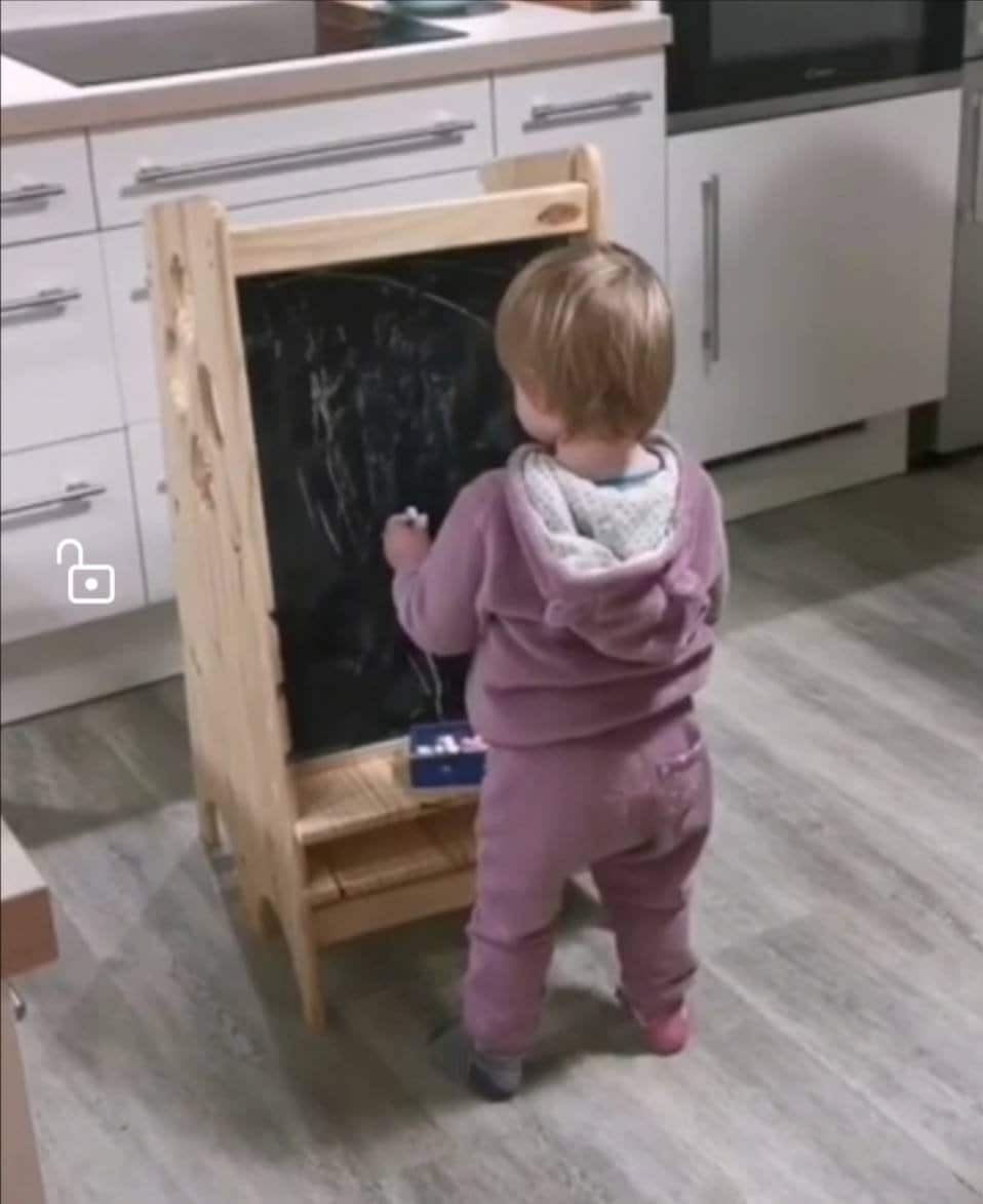 Enfant avec craie qui dessine sur le tableau de sa tour montessori